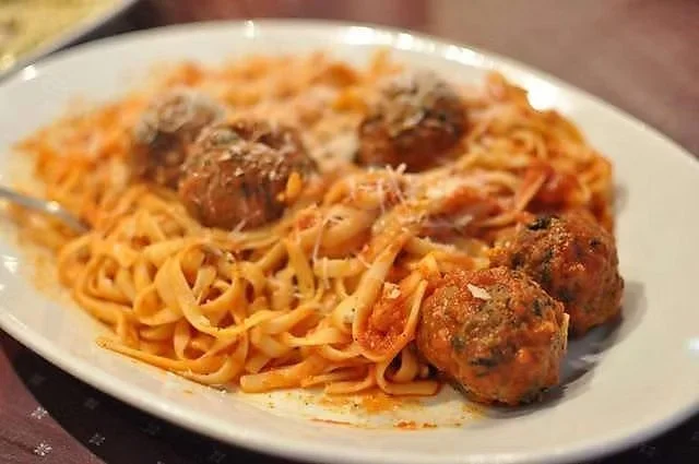 Plate of spaghetti with three meatballs topped with tomato sauce and grated cheese.