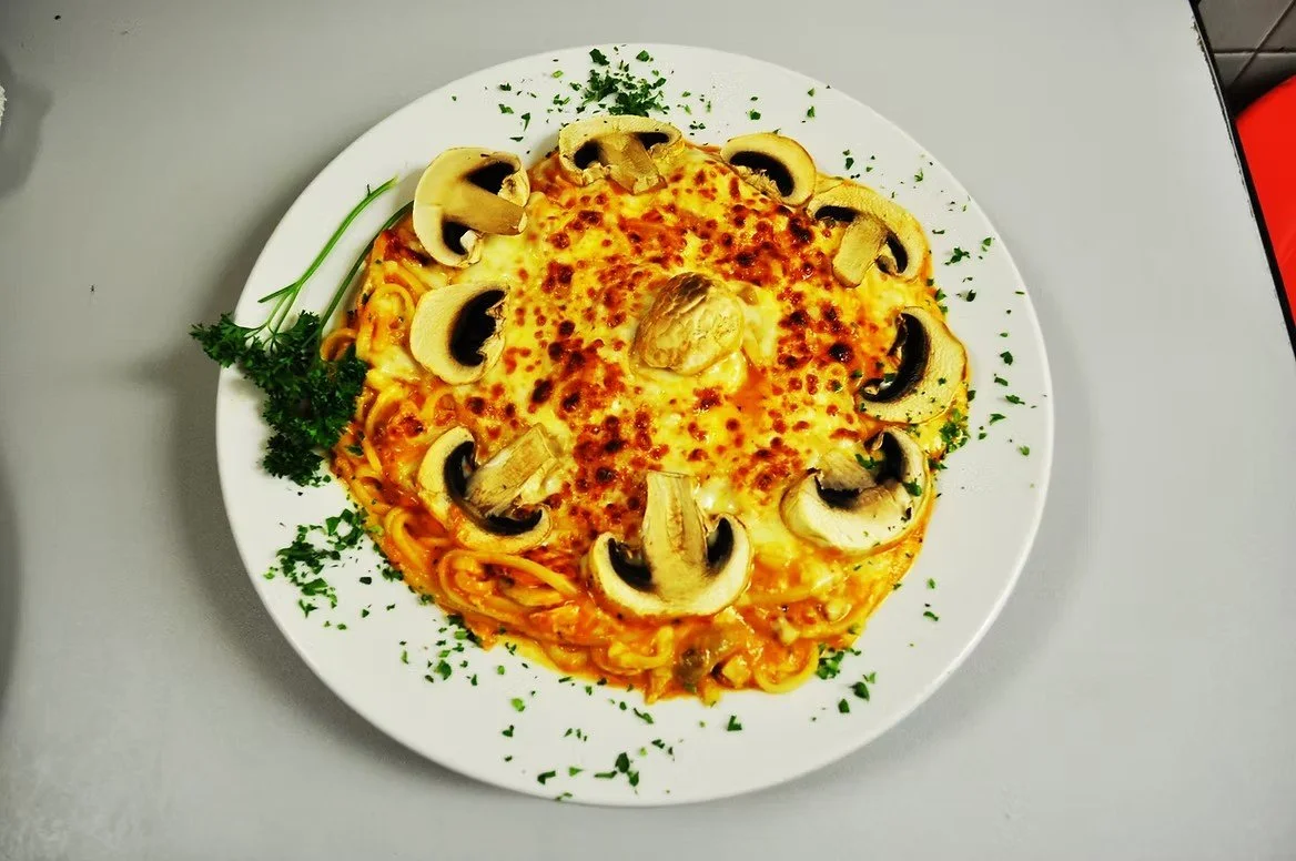 Plate of baked cheese and pasta with sliced mushrooms and a parsley garnish.