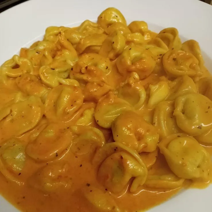 A plate of tortellini pasta covered in a creamy orange cheese sauce.