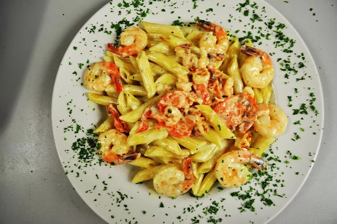 Plate of creamy shrimp and pasta garnished with chopped herbs.