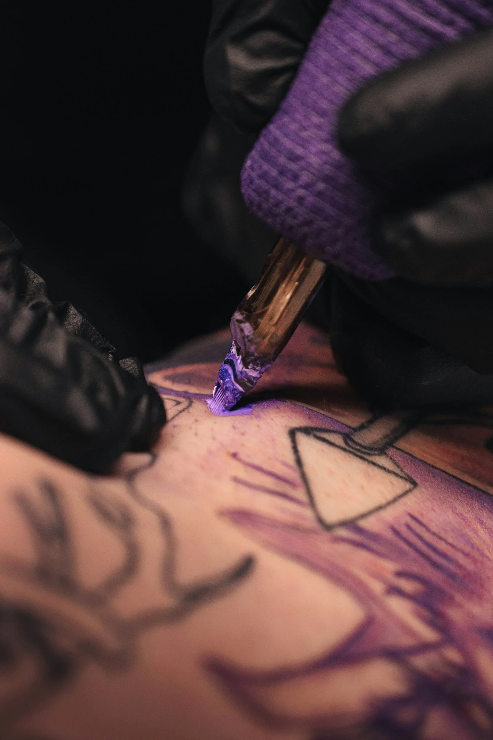 Close-up of a tattoo being inked with a purple tattoo machine, with the person's skin and part of the tattoo visible.