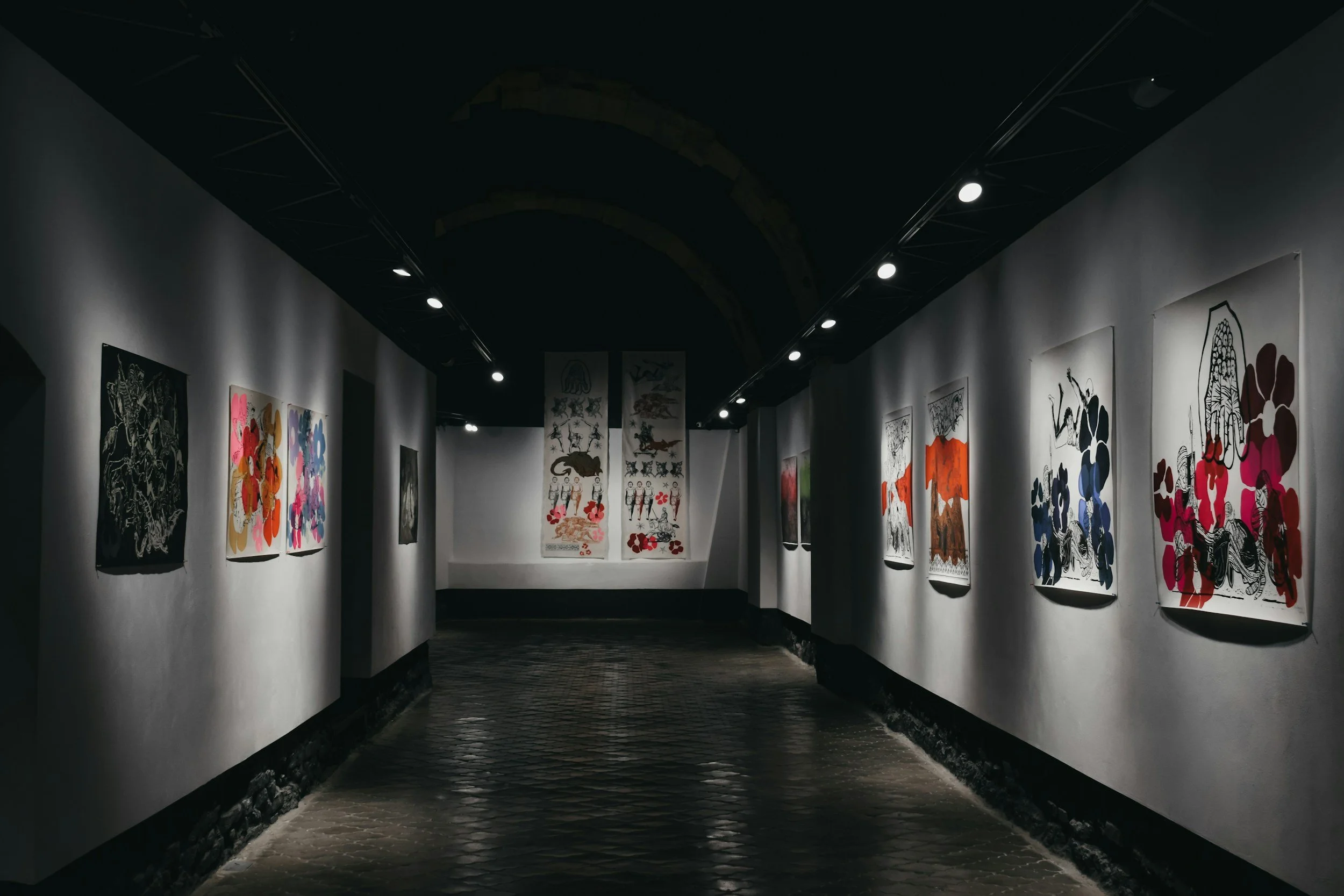 Art gallery with illuminated paintings on white walls and a dark ceiling in a dimly lit corridor.