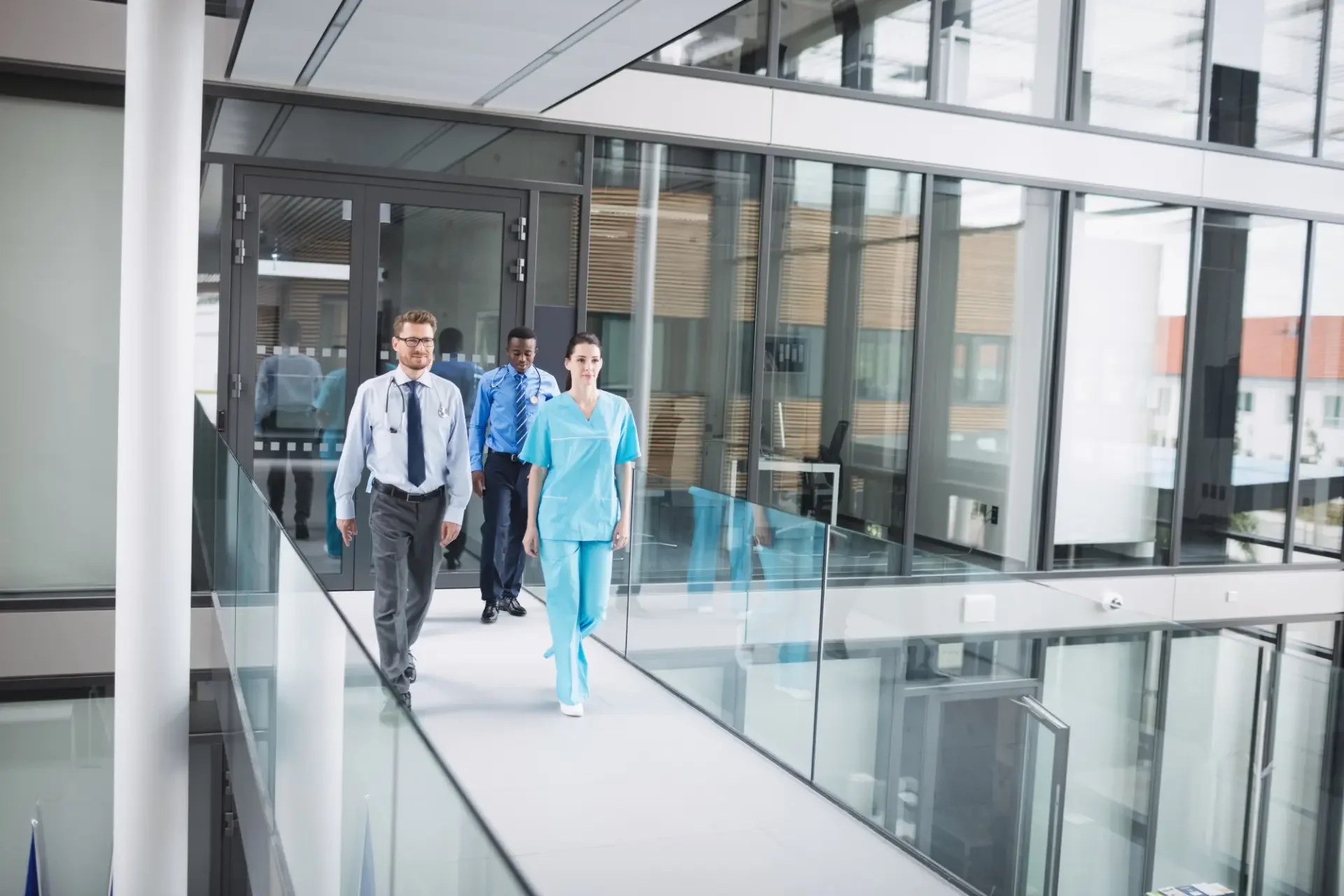 Healthcare professionals walking through a modern hospital corridor with glass walls and doors.