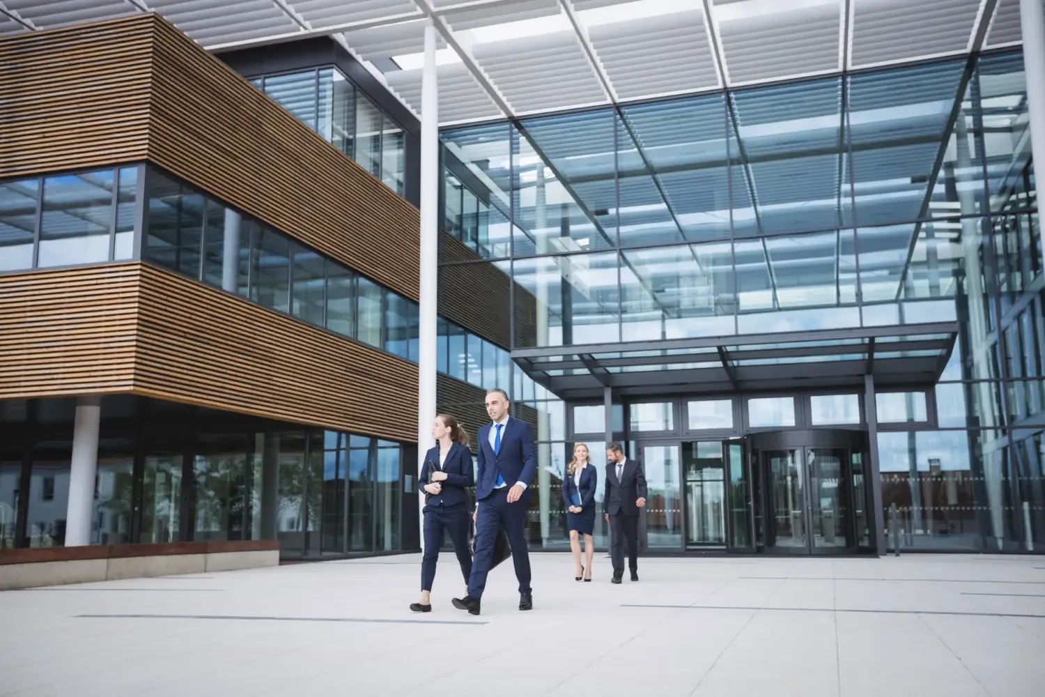 Business professionals walking out of a modern office building with glass and wood exterior.