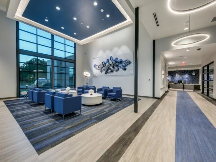 Modern hotel lobby with blue seating area, abstract wall art, large windows, and stylish lighting fixtures.