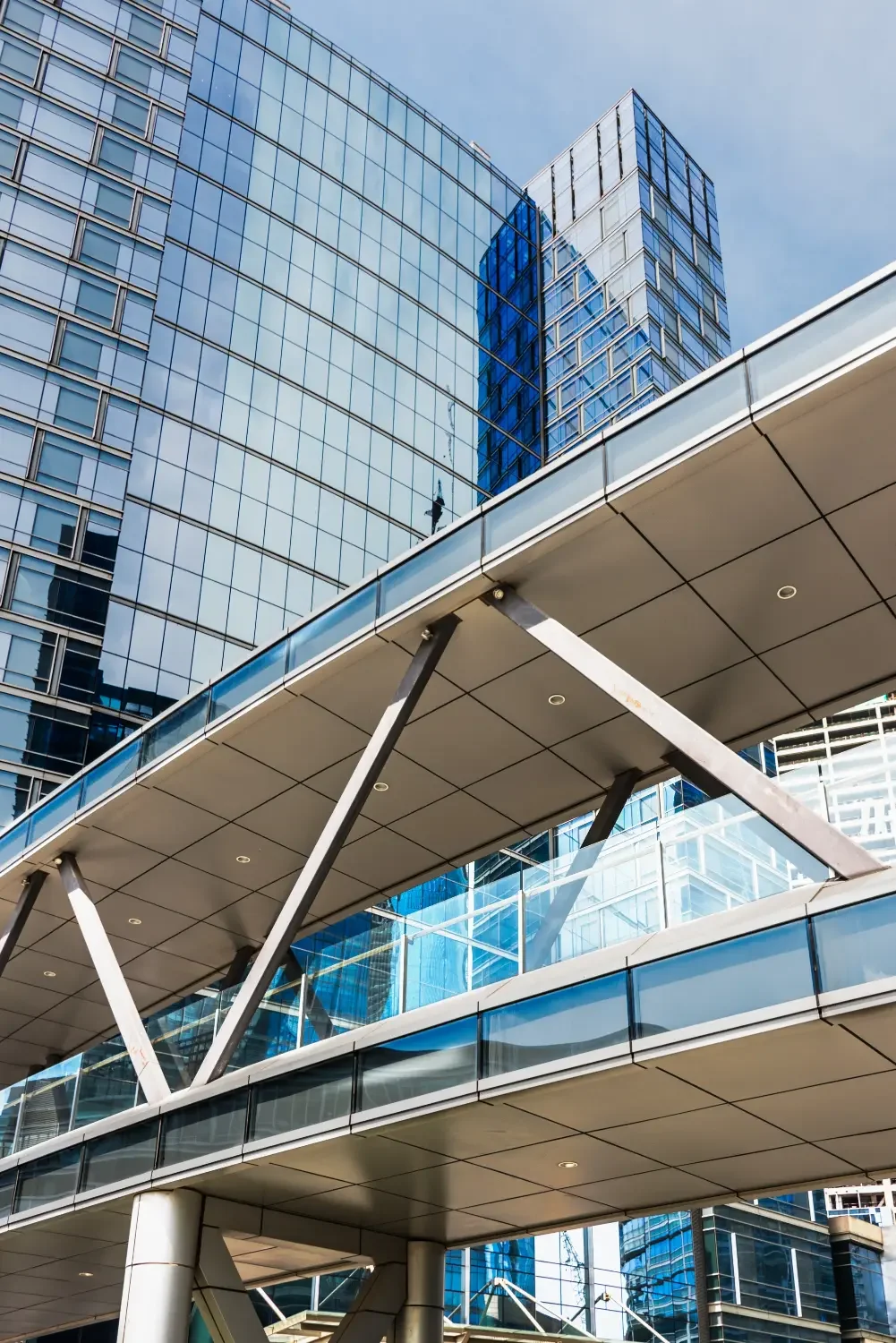 Modern glass skyscrapers with reflective windows and a skywalk connecting the buildings.
