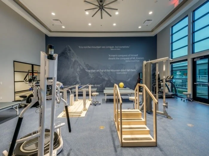 Fitness room with exercise equipment, wooden stairs, and a mountain-themed mural on the wall with inspirational quotes.