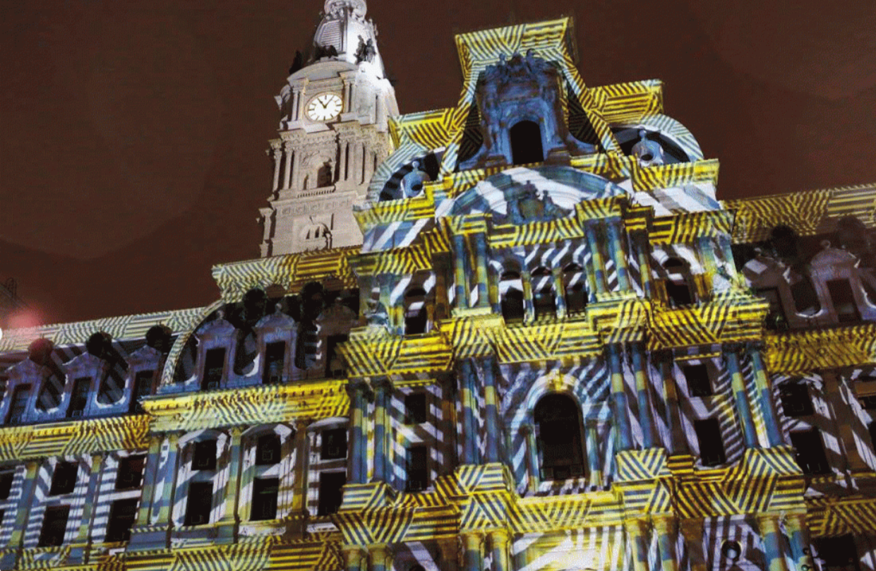 The historic building's facade is illuminated with vibrant, colorful light projections during a night event, creating a dynamic visual display.