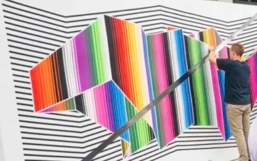 Person painting colorful geometric pattern on a wall with black and white stripes.