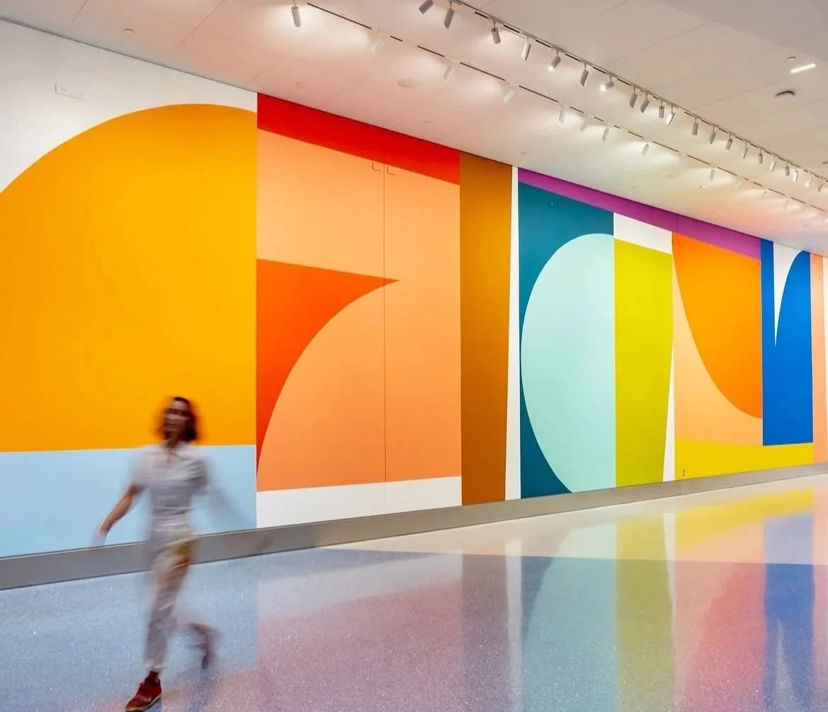 A woman walking inside a modern building with colorful abstract wall art and a shiny floor.