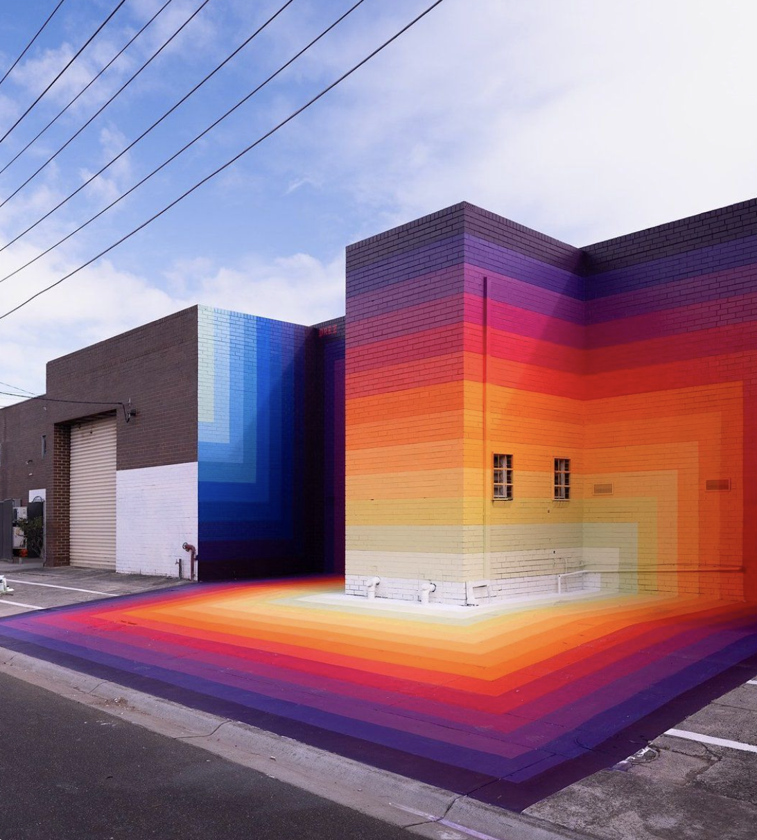 A building with a rainbow mural painted on its walls and ground.