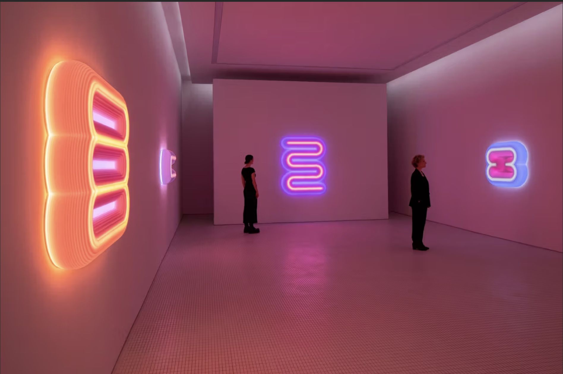 Interior of an art gallery with pink and purple neon signs on white walls, two women observing the artwork.