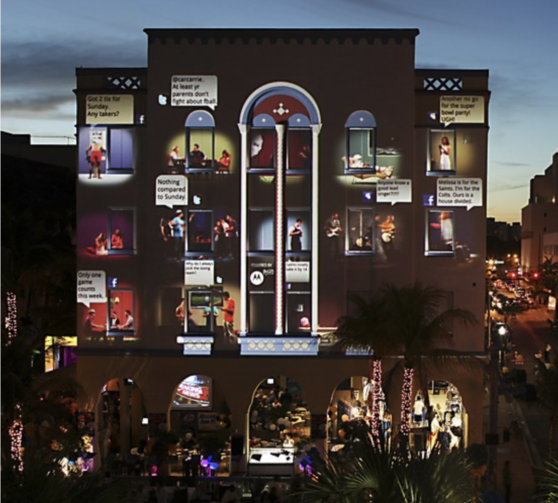 Building decorated with lights and a large vertical thermometer, with animated figures and speech bubbles advertising events.