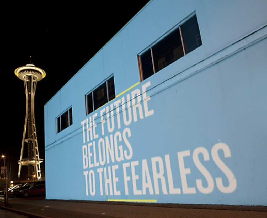 Nighttime mural on a building that reads, "THE FUTURE BELONGS TO THE FEARLESS." In the background, the Space Needle is illuminated.