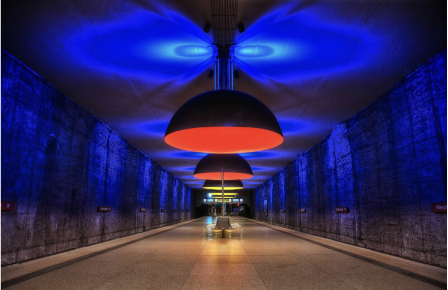 Underground subway station with blue, red, and yellow circular ceiling lights and a corridor leading to the platform.