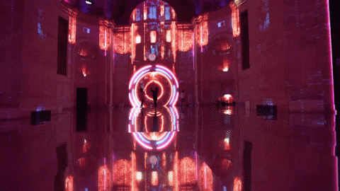 Silhouette of two people standing under a neon-lit arch in a dimly lit room with pink and purple lighting.