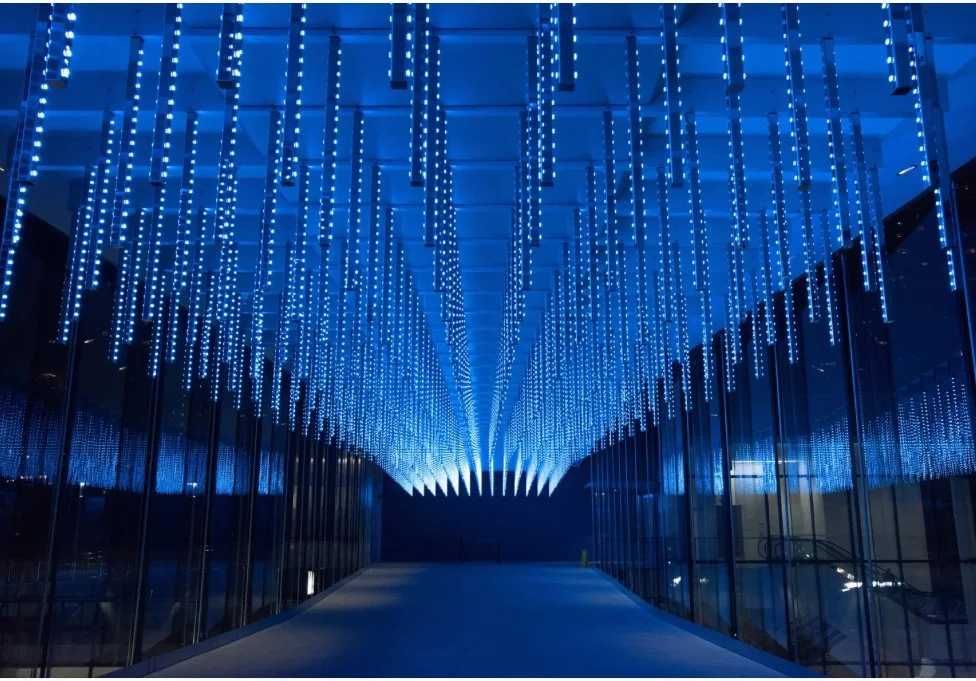 A modern, curved corridor with glass walls and blue LED light installation on the ceiling.