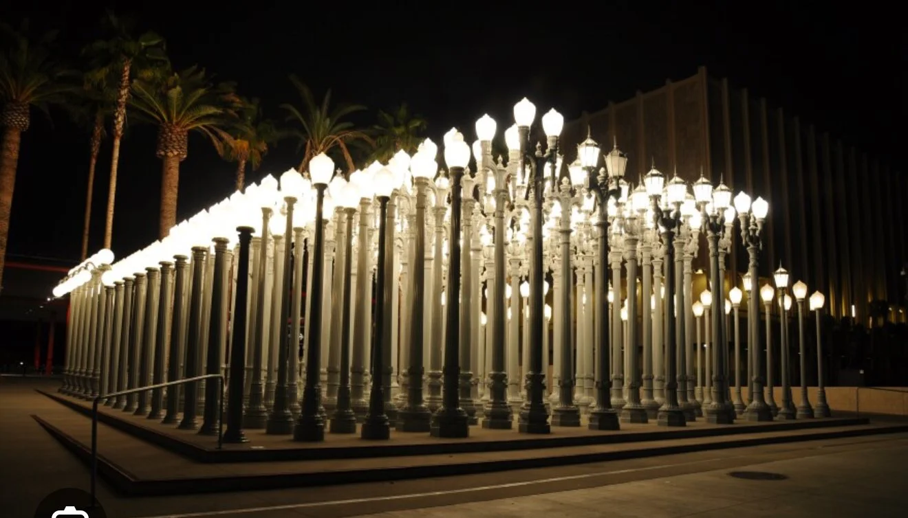 An art installation resembling a streetlight formation with numerous illuminated street lights on tall poles, arranged in a rectangular shape at night.