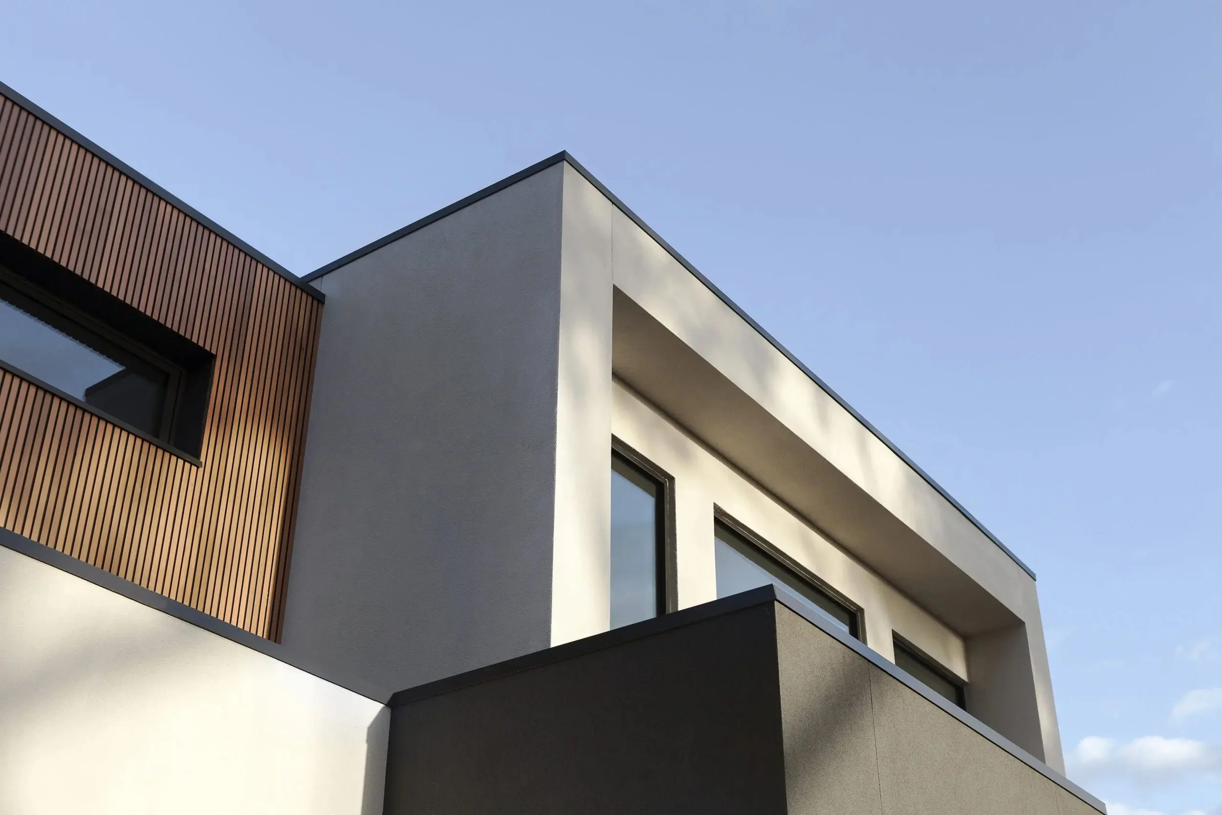 Close-up of modern building with white, black, and wooden exterior panels, and rectangular windows under a clear blue sky.