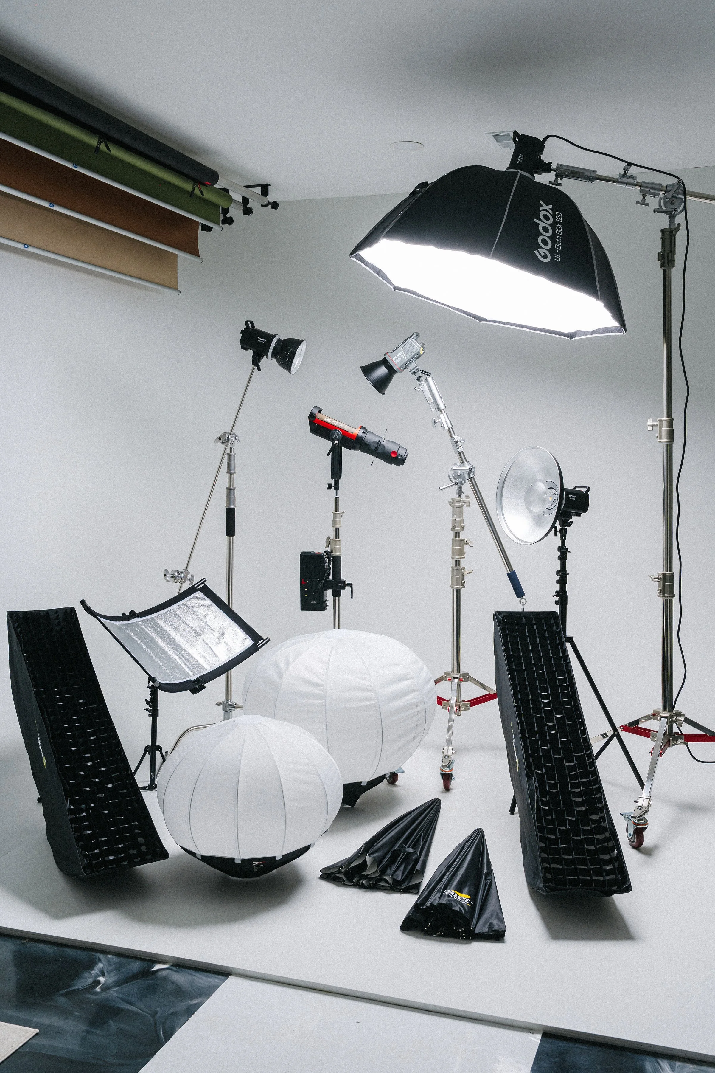 Photography studio setup with lights, softboxes, reflectors, umbrellas, and backdrop support in a white cyclorama.