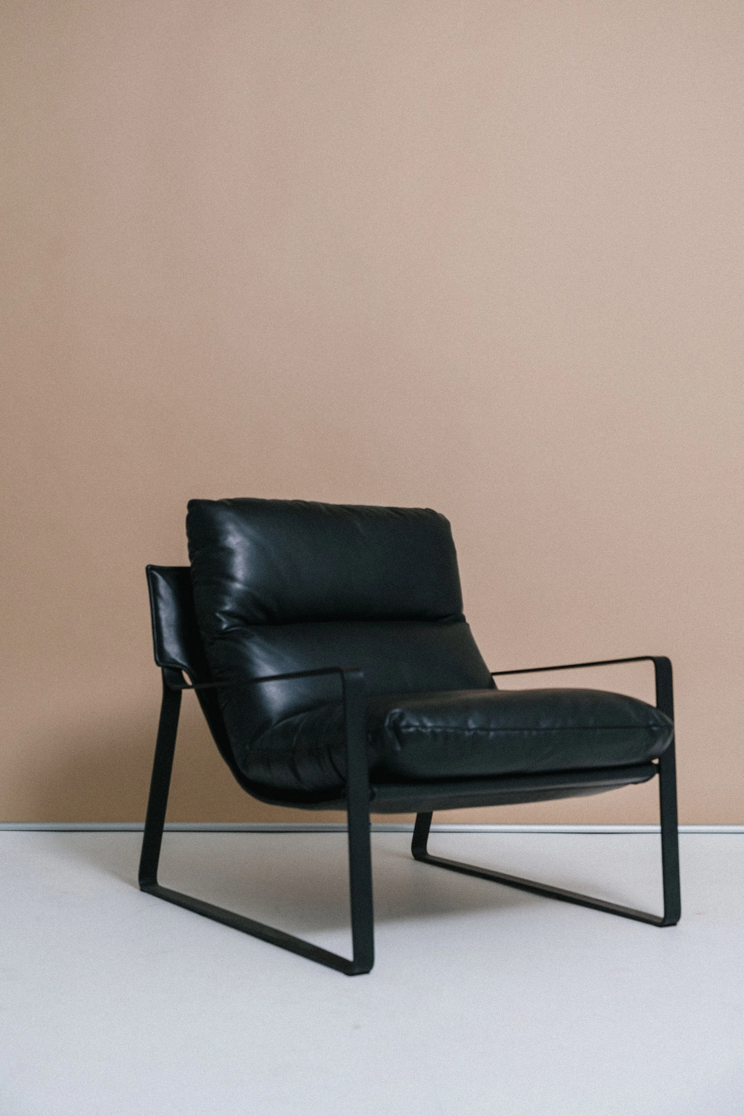 A black leather lounge chair with metal frame in front of a beige wall and white carpet.