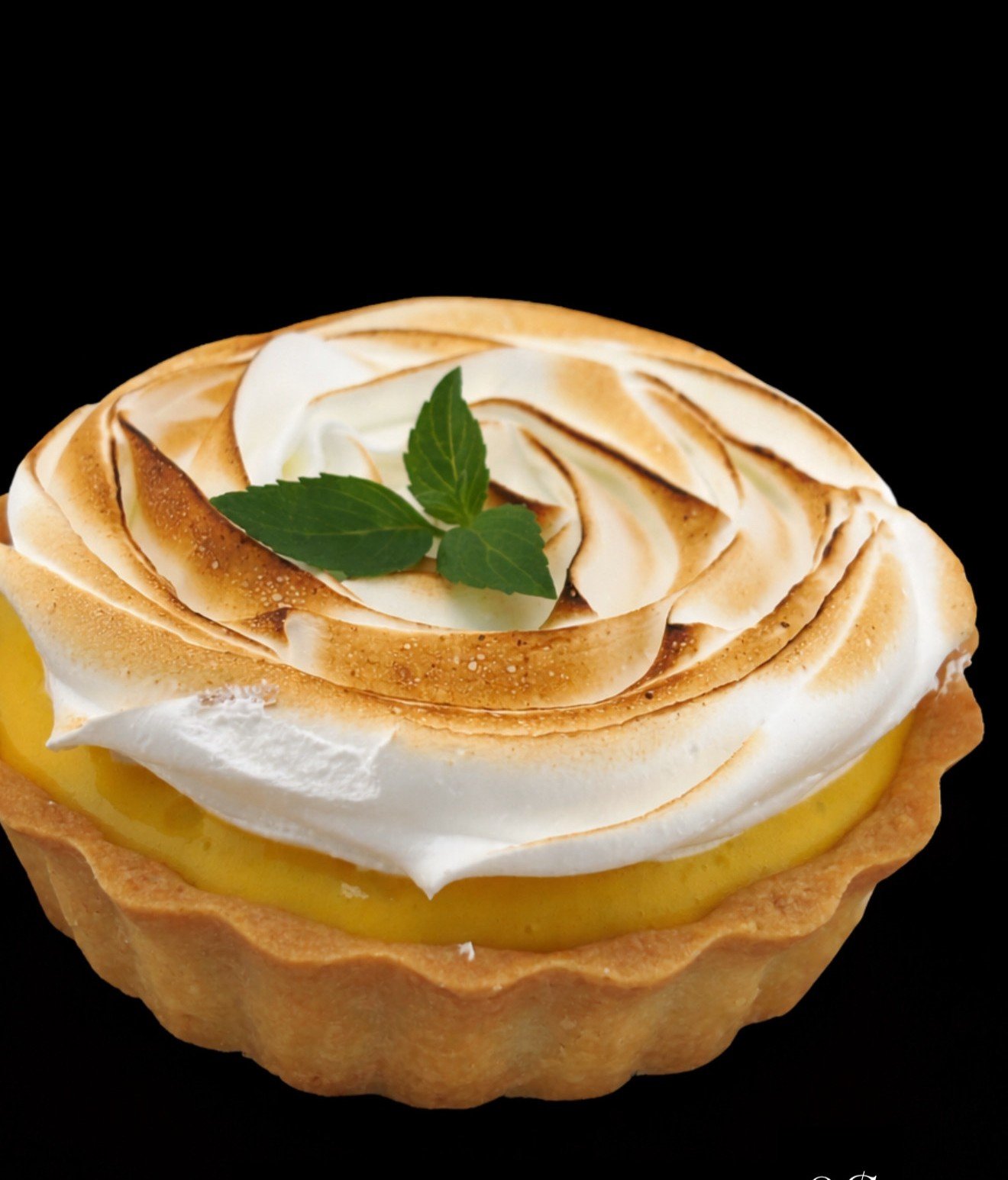 Lemon tart with toasted meringue topping and fresh mint leaves on top, against a black background.