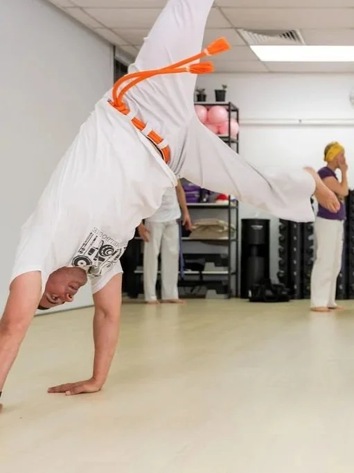 Person performing a cartwheel in a fitness studio with others in the background.