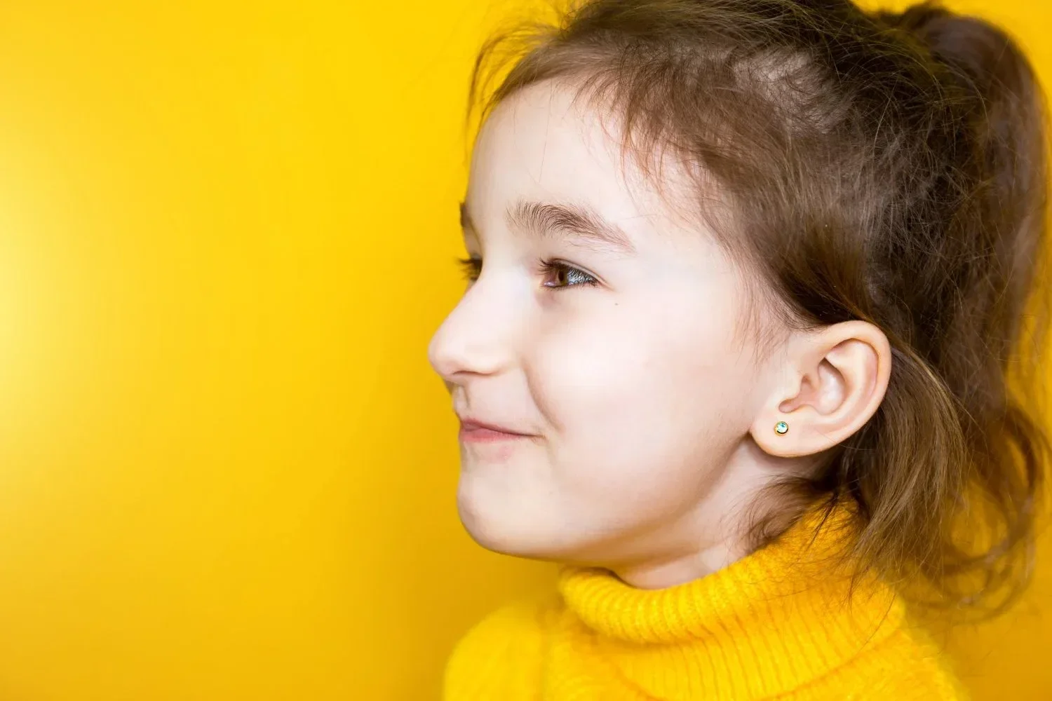Profile of a smiling child in a yellow sweater against a bright yellow background. The mood is cheerful and vibrant, matching the vivid backdrop.