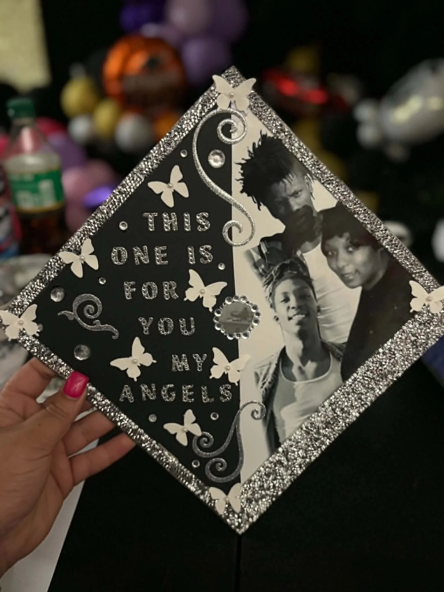 Close-up of a decorated photo frame with the text 'This one is for you Angeles' and a black-and-white picture of three people. The frame is adorned with butterflies and rhinestones.