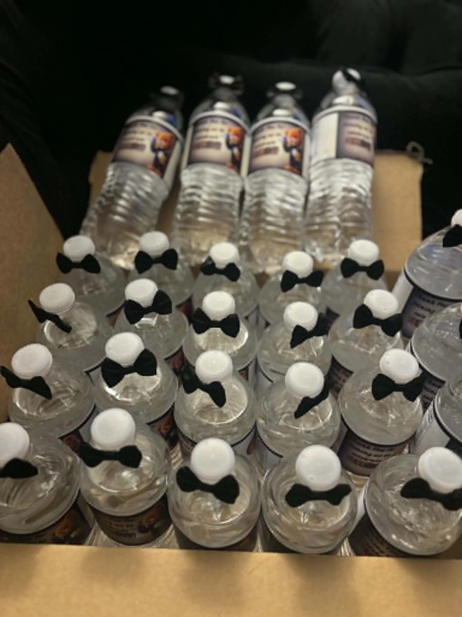 Multiple water bottles with black bowtie decorations on their caps, arranged in rows on a table or display surface.