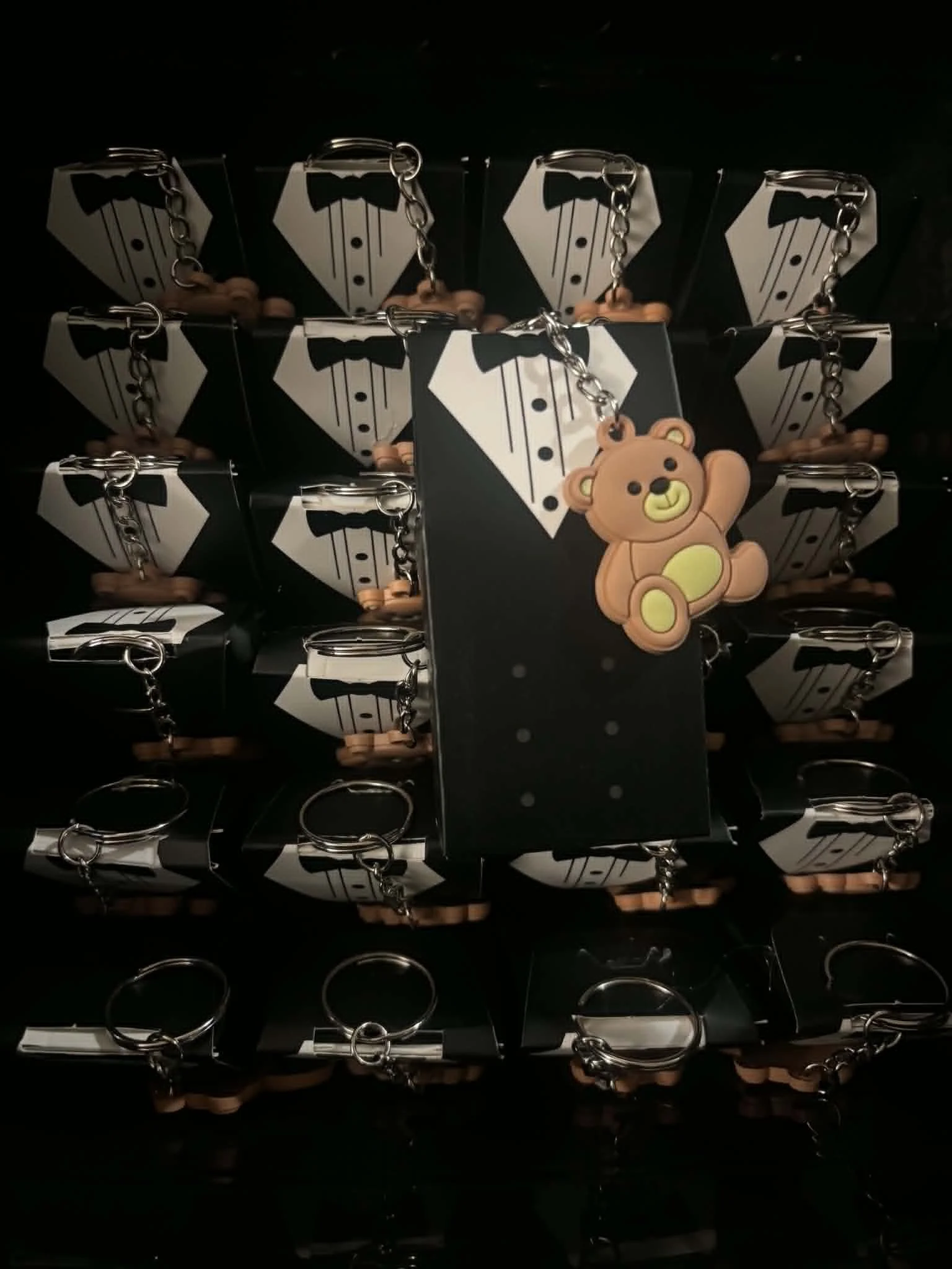 Multiple small boxes with tuxedo and bowtie design, each attached to a keychain, arranged in a grid. One keychain features a teddy bear plush toy.