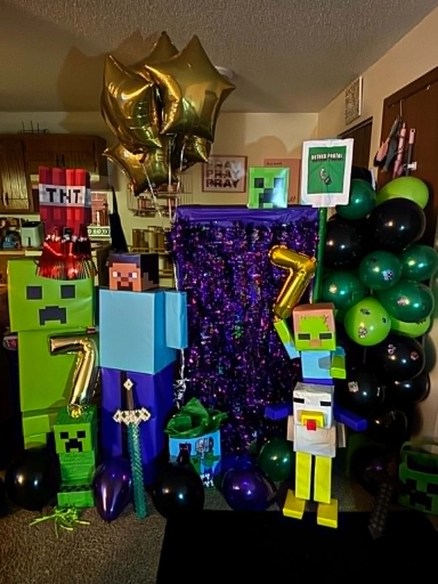 Minecraft-themed birthday party decorations with green, black, and purple balloons, pixel art blocks, gold star-shaped balloons, a purple sparkly tablecloth, and a variety of Minecraft character cutouts and signs.
