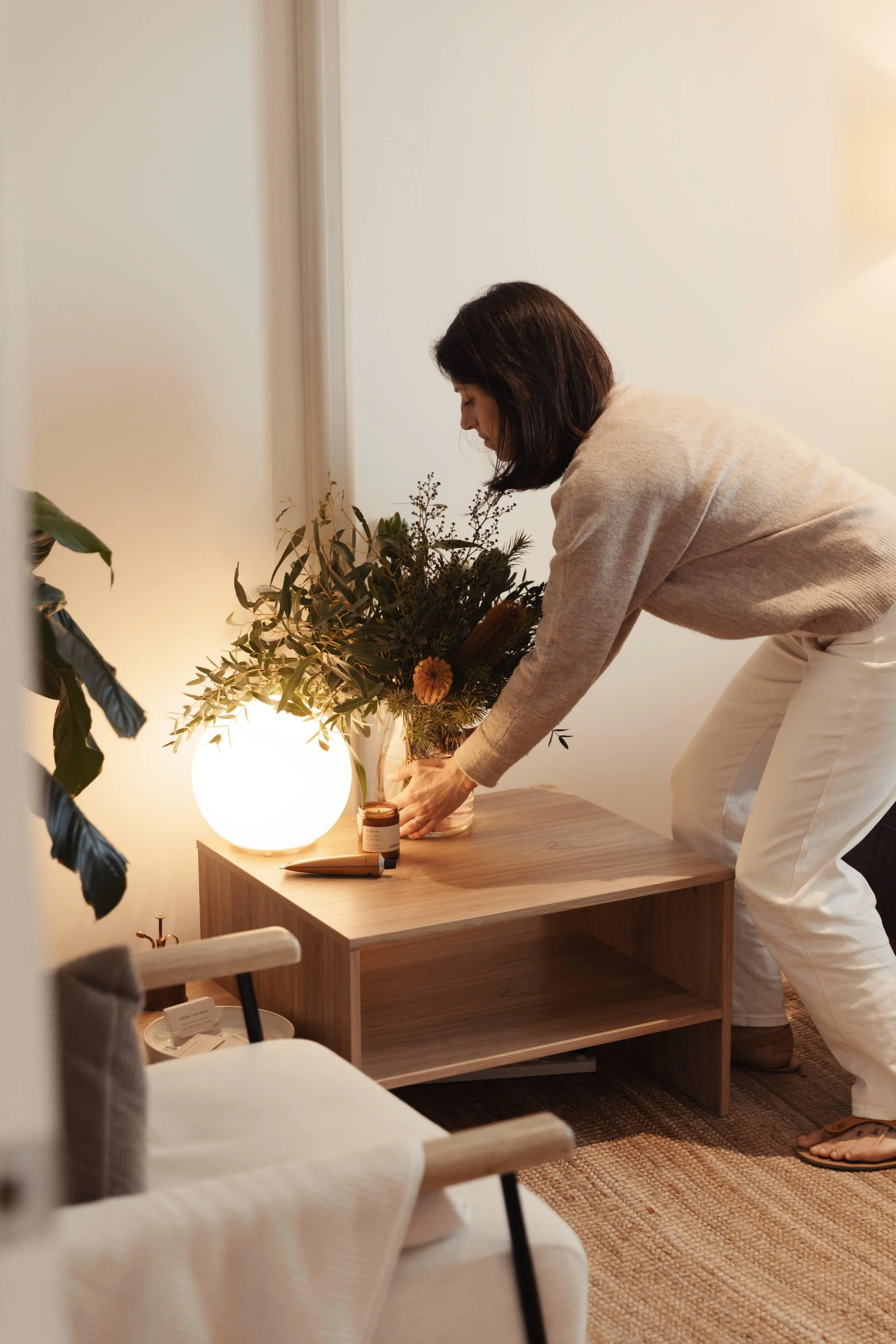 Somatic nutrition therapist and dietitian Emily Hahn arranging a flower bouquet on a wooden table near a glowing lamp, with a candle, in a cozy therapy room.