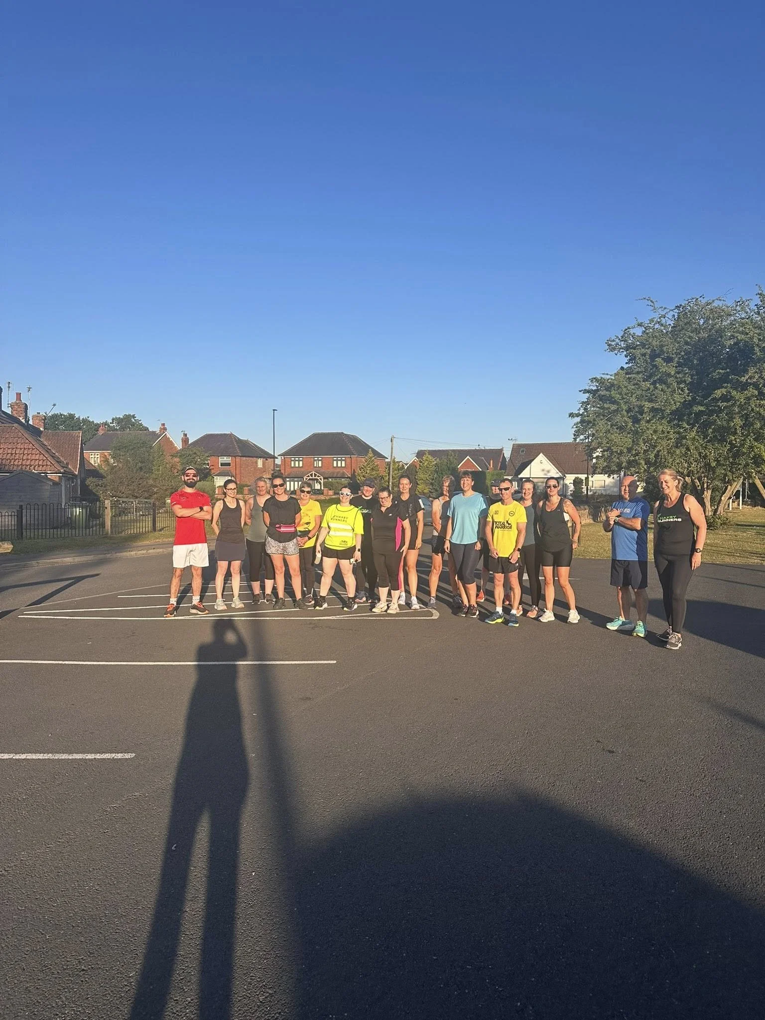 Group of people standing in a parking lot on a sunny day, with houses and trees in the background.