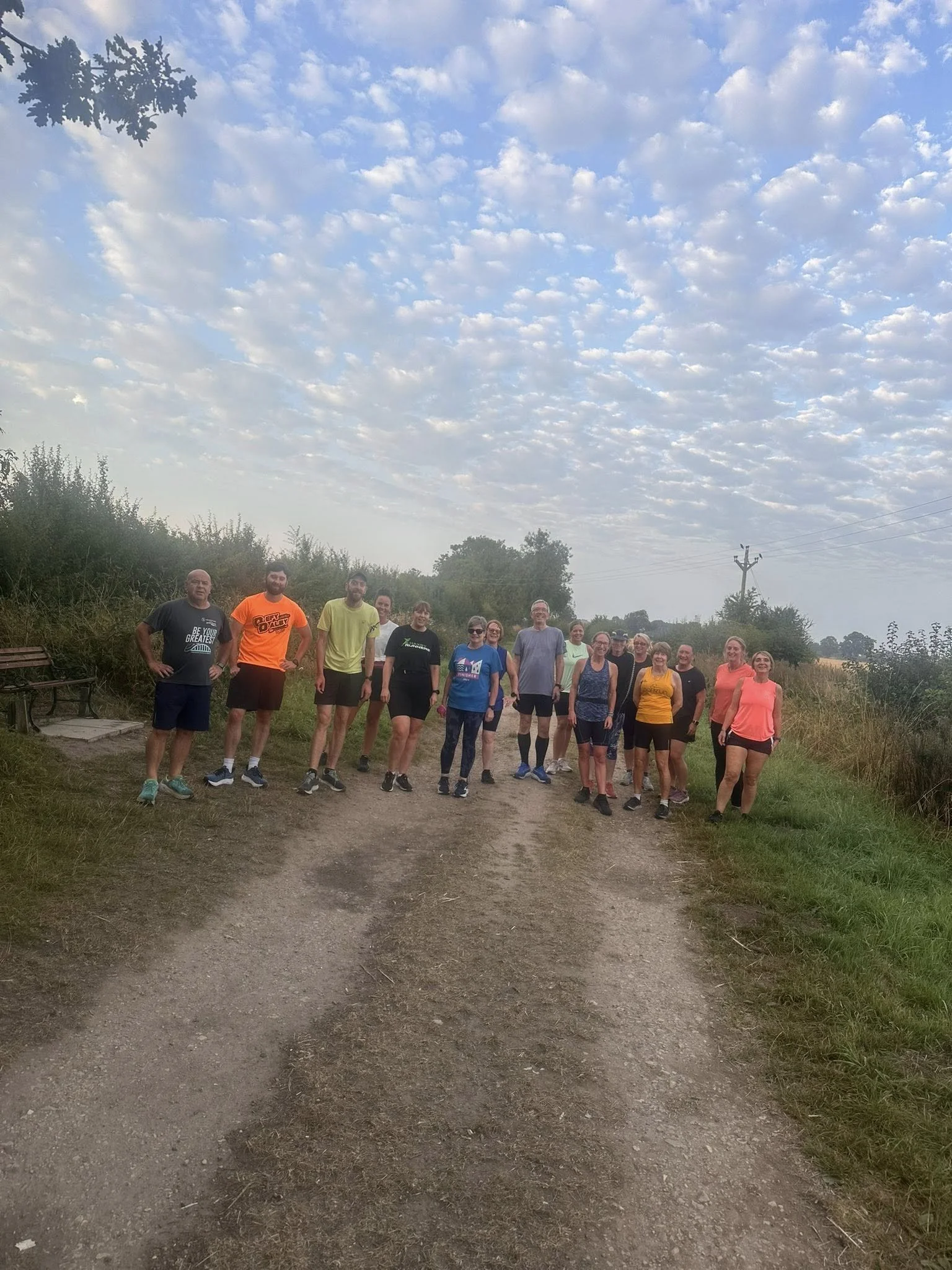 Group of people standing on a dirt path in a rural area with cloudy sky overhead during early morning or late evening.