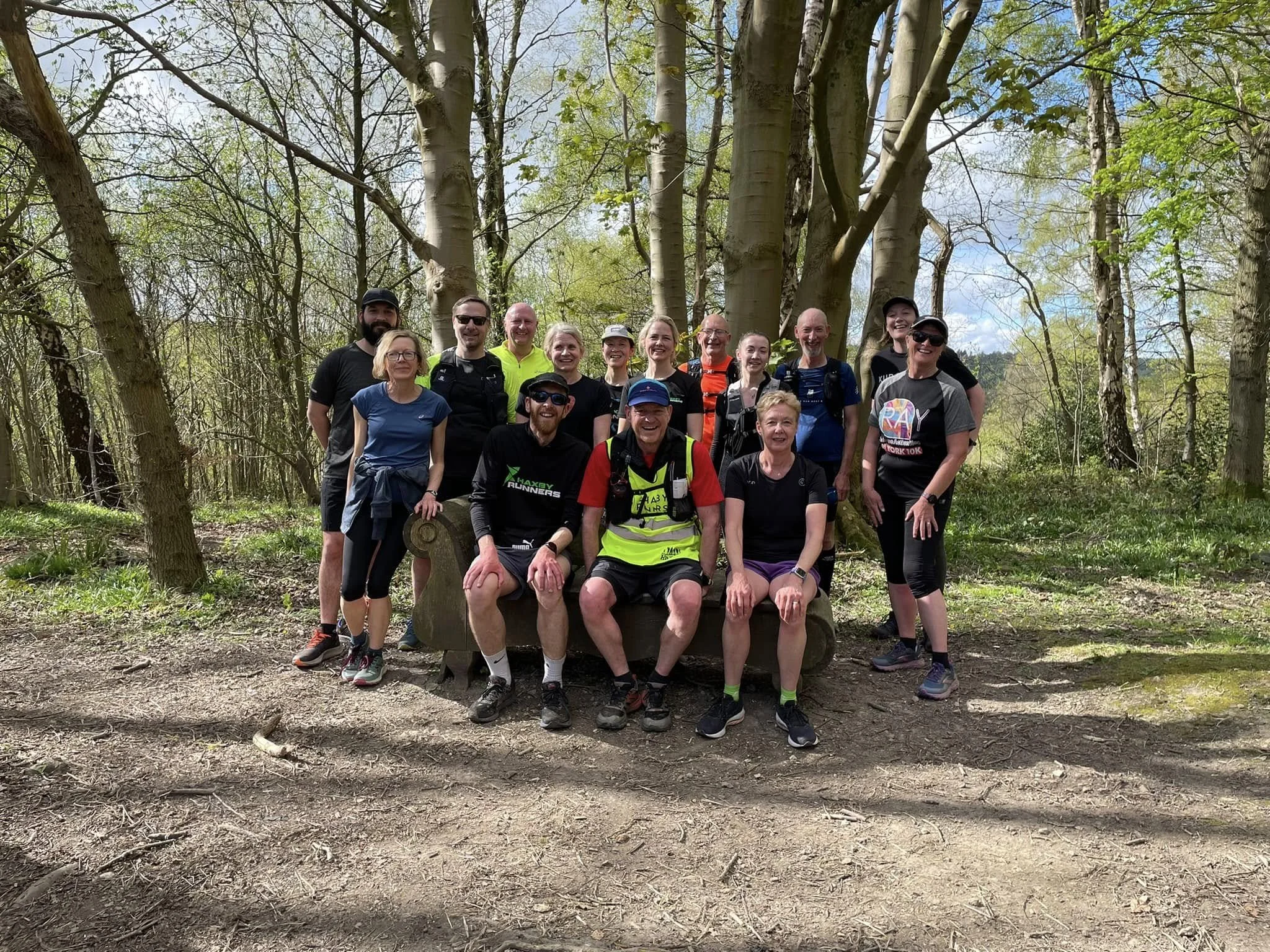 Group of people posing in a forest during a hike, standing and sitting on a wooden bench.