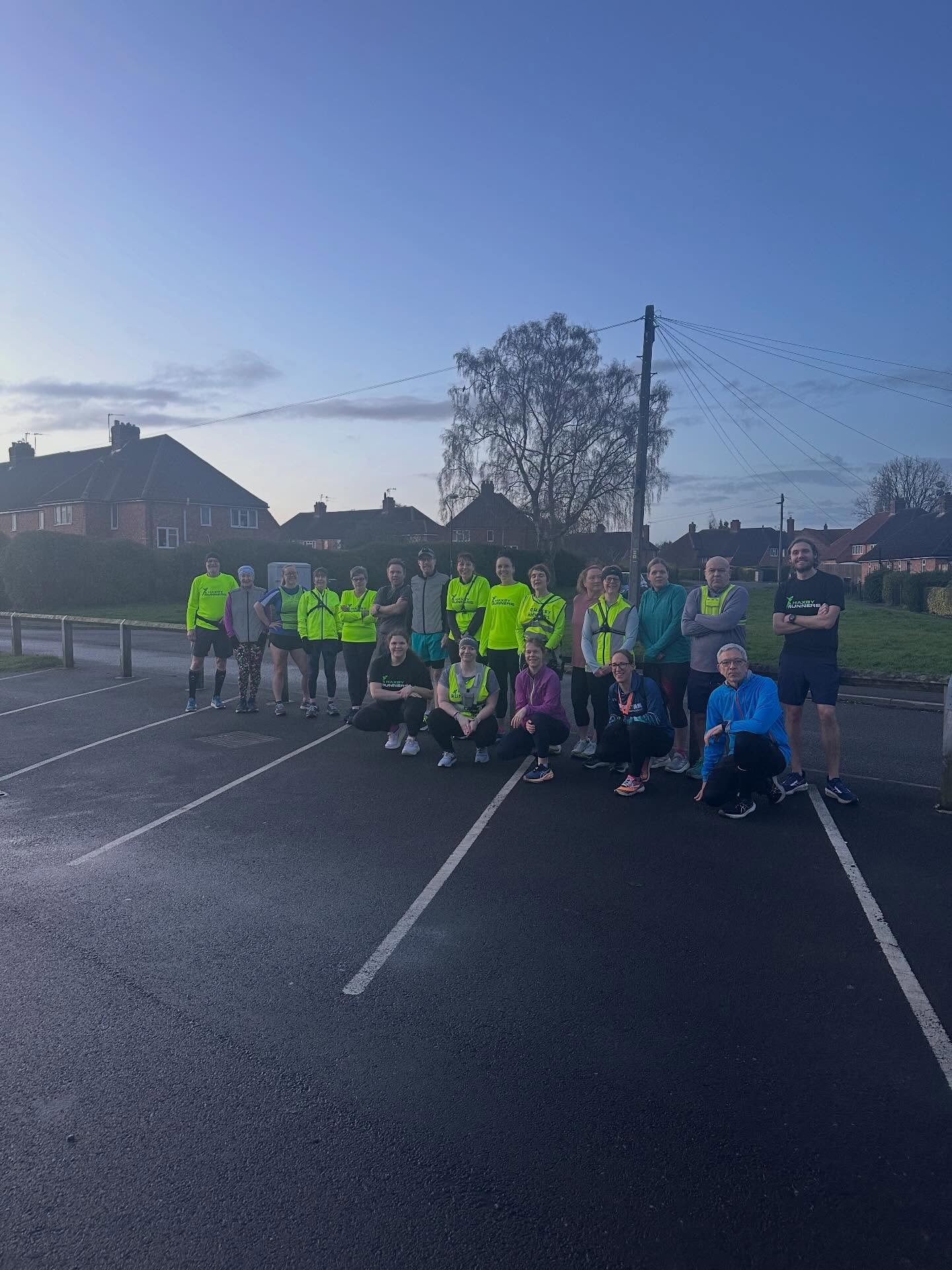 Group of runners in reflective gear and athletic clothing gathered in a parking lot during dusk.