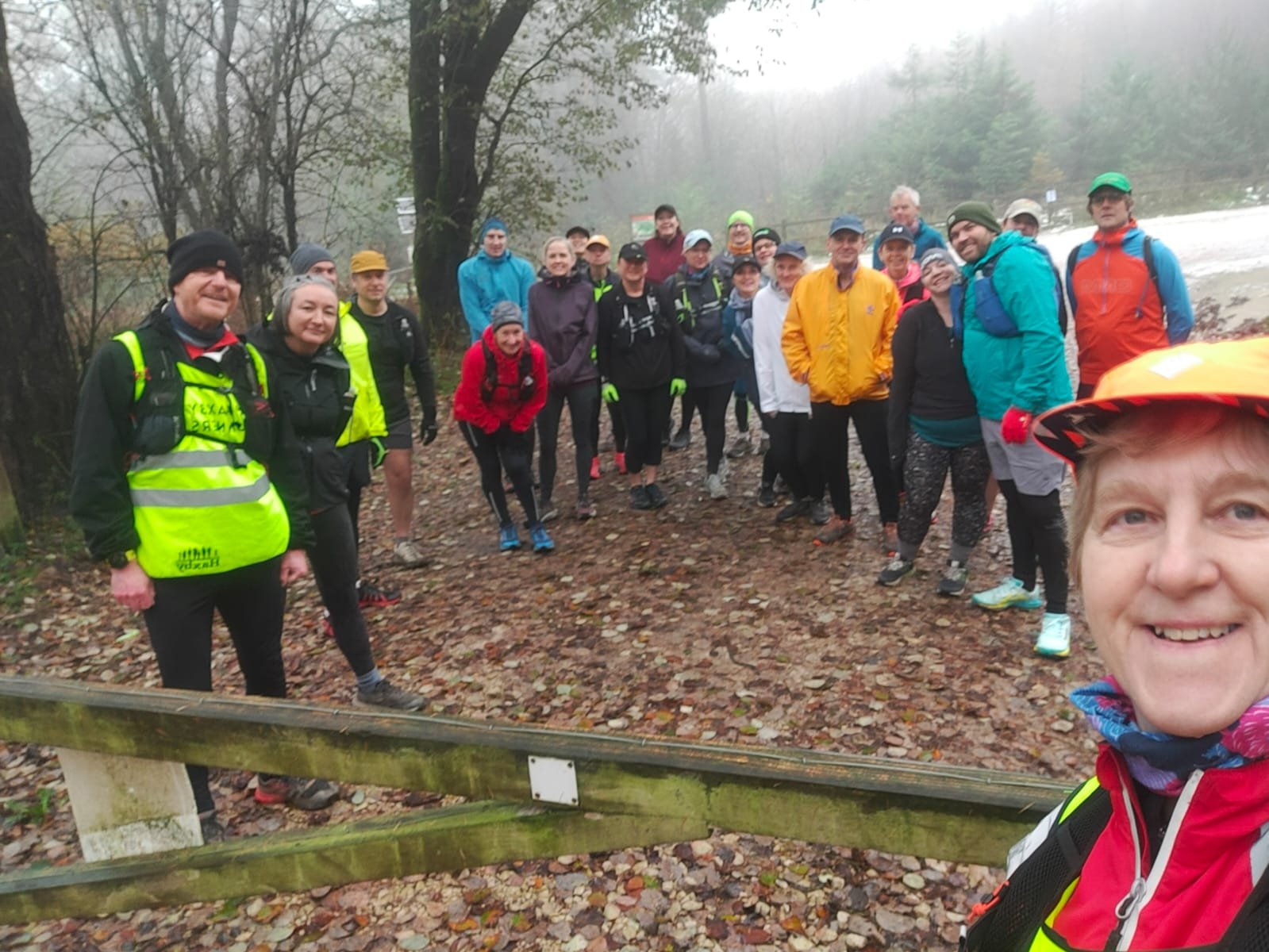 A group of people dressed in outdoor gear and reflective vests gathering on a muddy trail in a foggy forest.