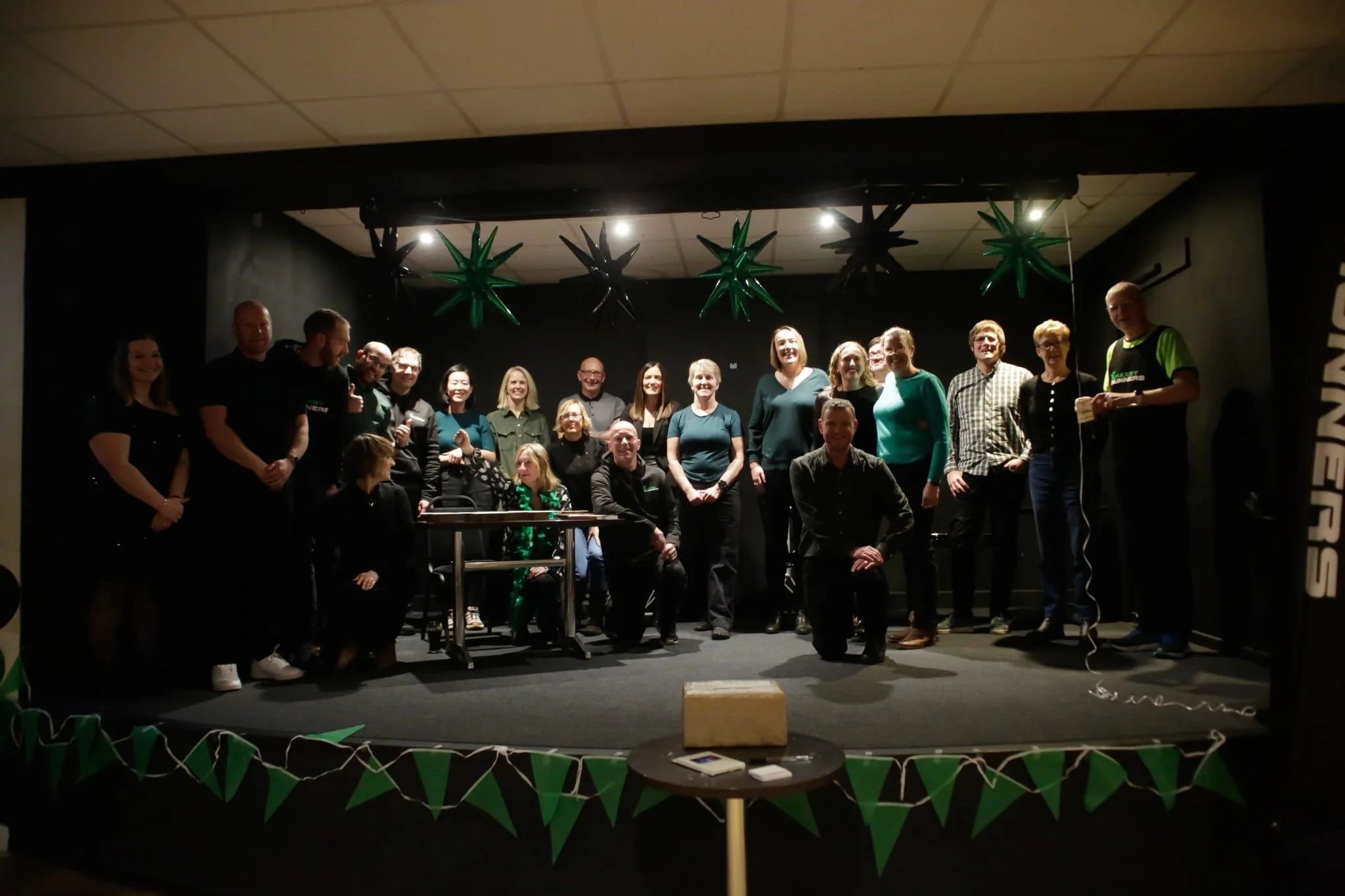 Group of people on a stage celebrating, with green and black star-shaped balloons hanging from the ceiling.