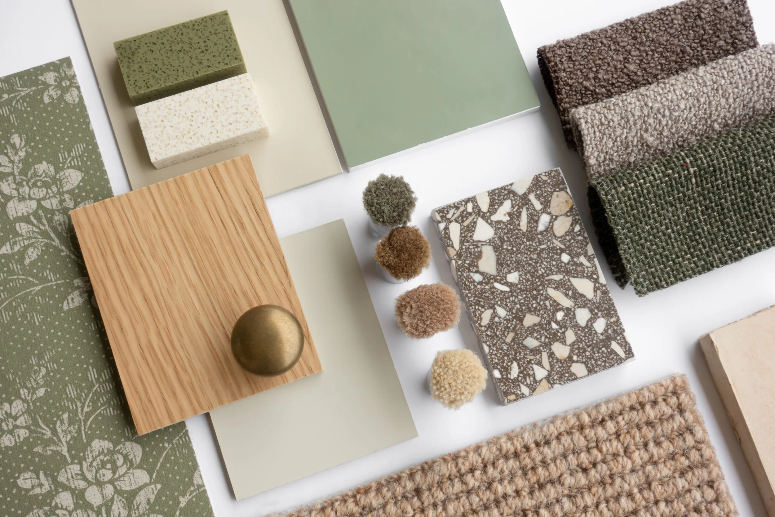 Samples of various textures, colors, and materials including fabric swatches, tiles, wood, a metal ball, and small fuzzy objects arranged on a white surface for design or decor inspiration.