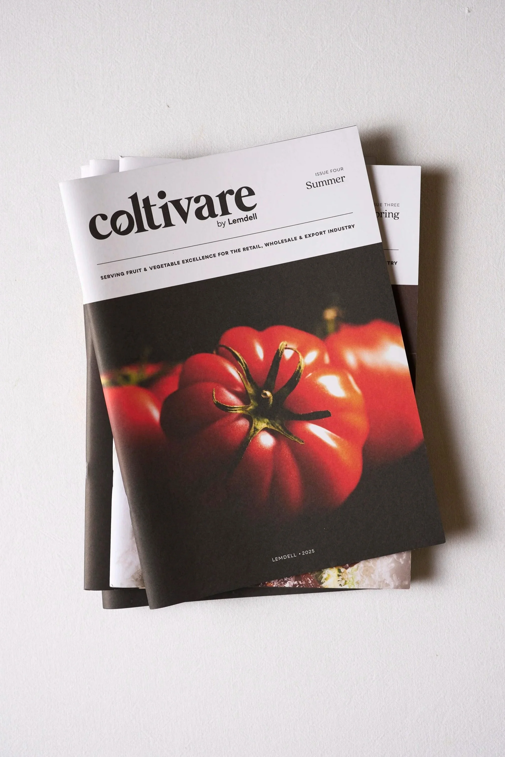 Stacked magazines on a white surface, with the top magazine titled "Cultivate" featuring a close-up of red tomatoes on the cover.
