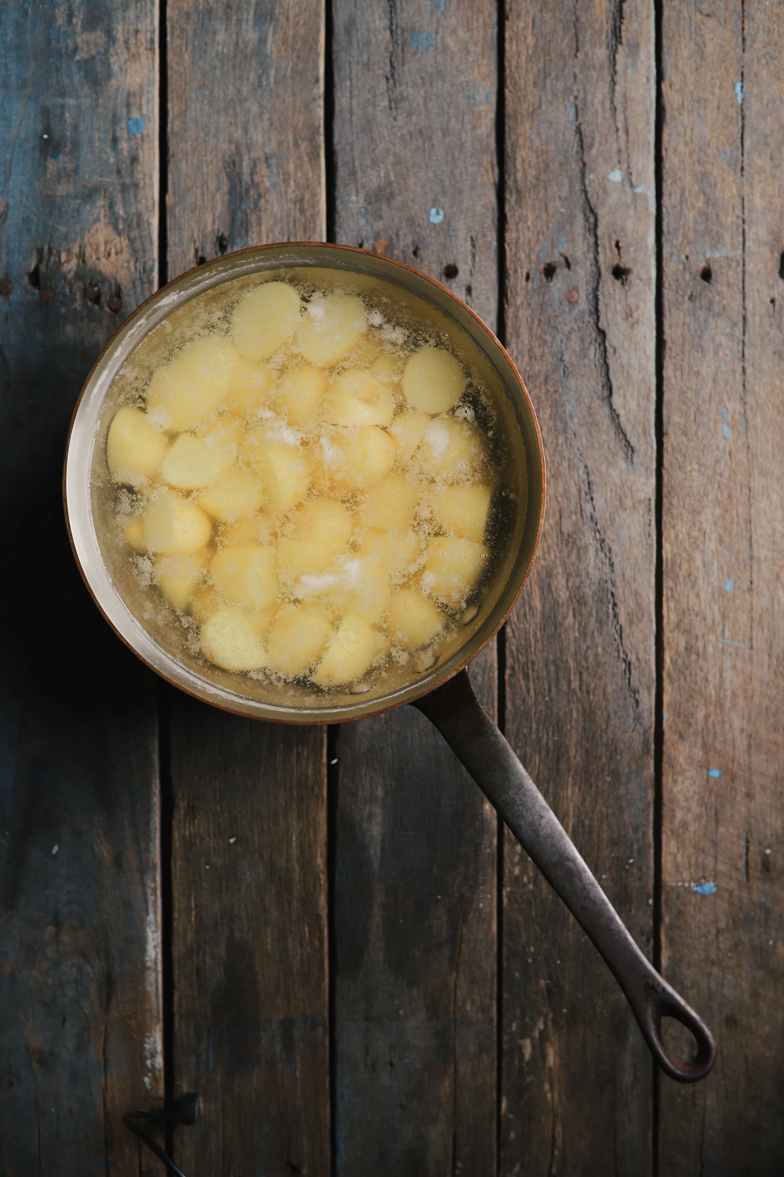 A pot of boiling yellow potatoes on a distressed wooden surface.