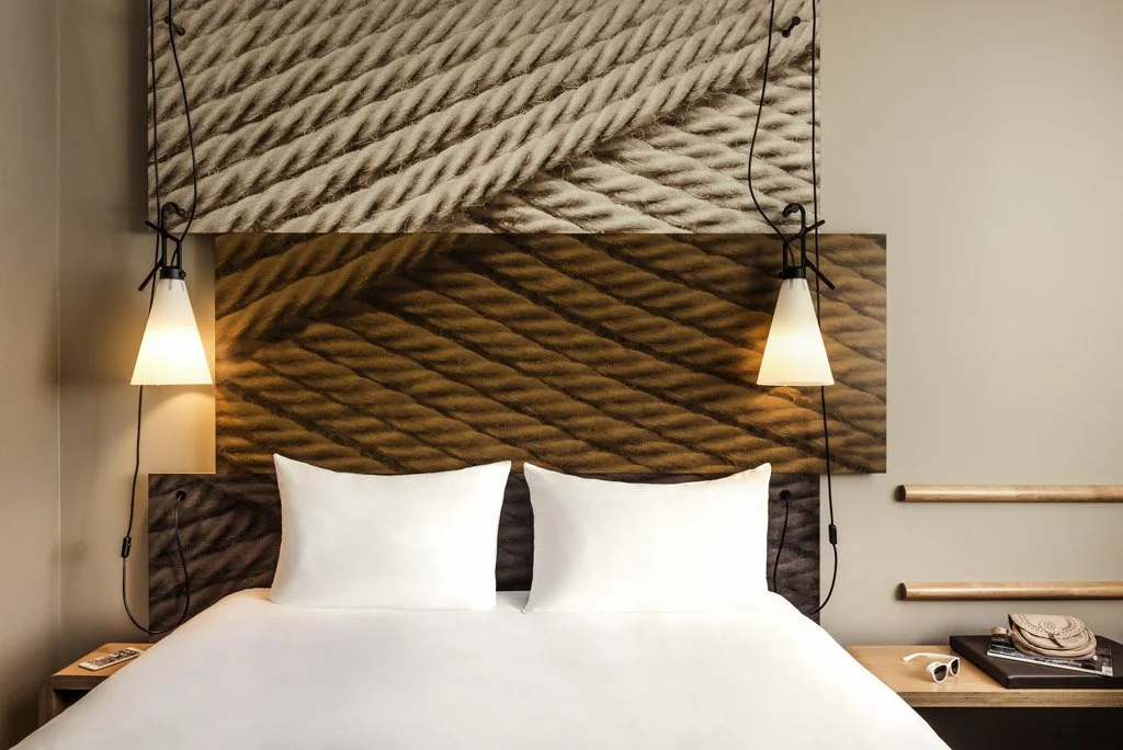 A bedroom with a headboard featuring a large rope design, two white pillows, and two wall-mounted lights on either side.