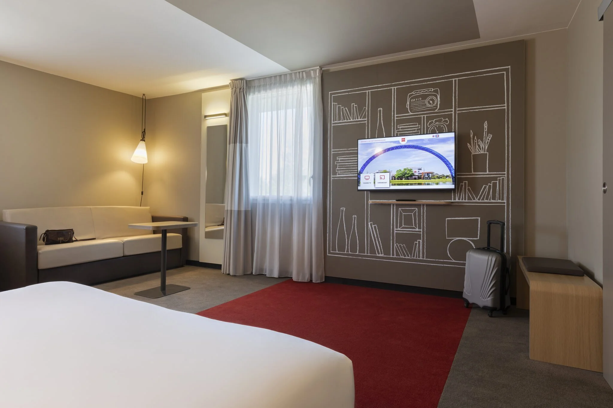 Salon d'hôtel avec un canapé blanc, une table, une télévision accrochée au mur avec un dessin de rayonnages et d'objets en blanc, une fenêtre avec rideaux blancs, un tapis rouge et un fauteuil gris.