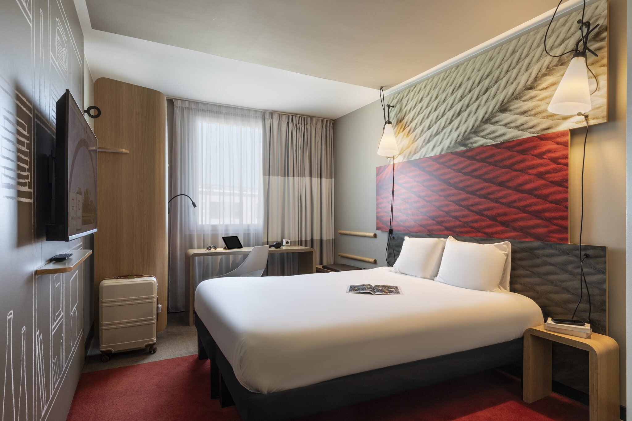 Chambre d'hôtel moderne avec un lit, une tête de lit décorée de corde, une lampe suspendue, une fenêtre avec rideaux, et un bureau avec un ordinateur portable.