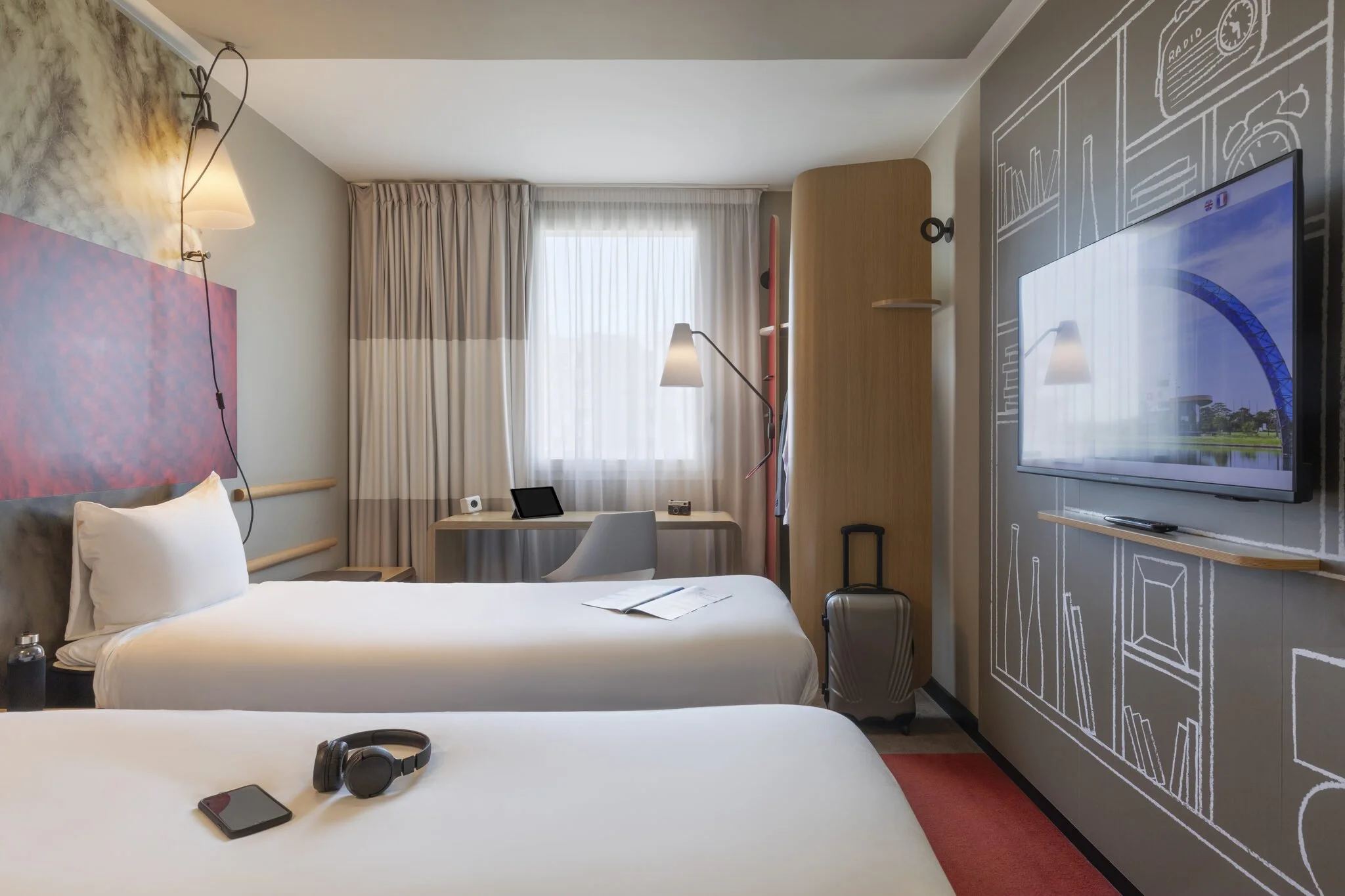 Chambre d'hôtel moderne avec lits faits, table de travail, télévision, et décor mural avec dessin de plans d'architecture.