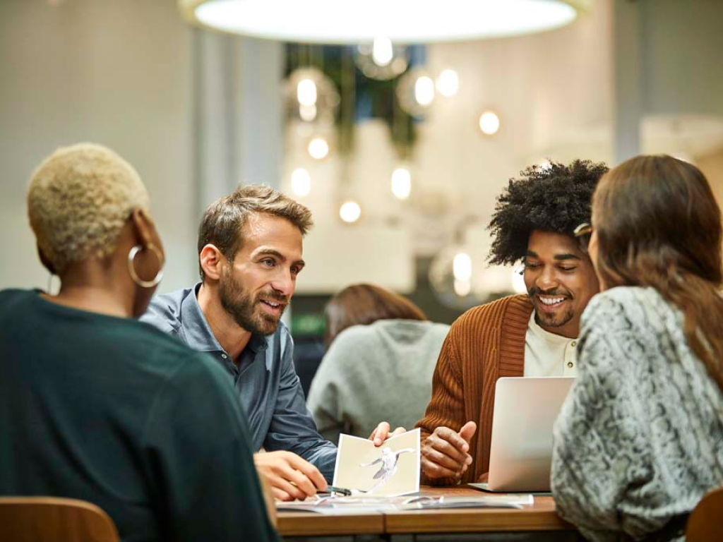 Group of four young adults sitting at a table having a conversation in a well-lit indoor setting.