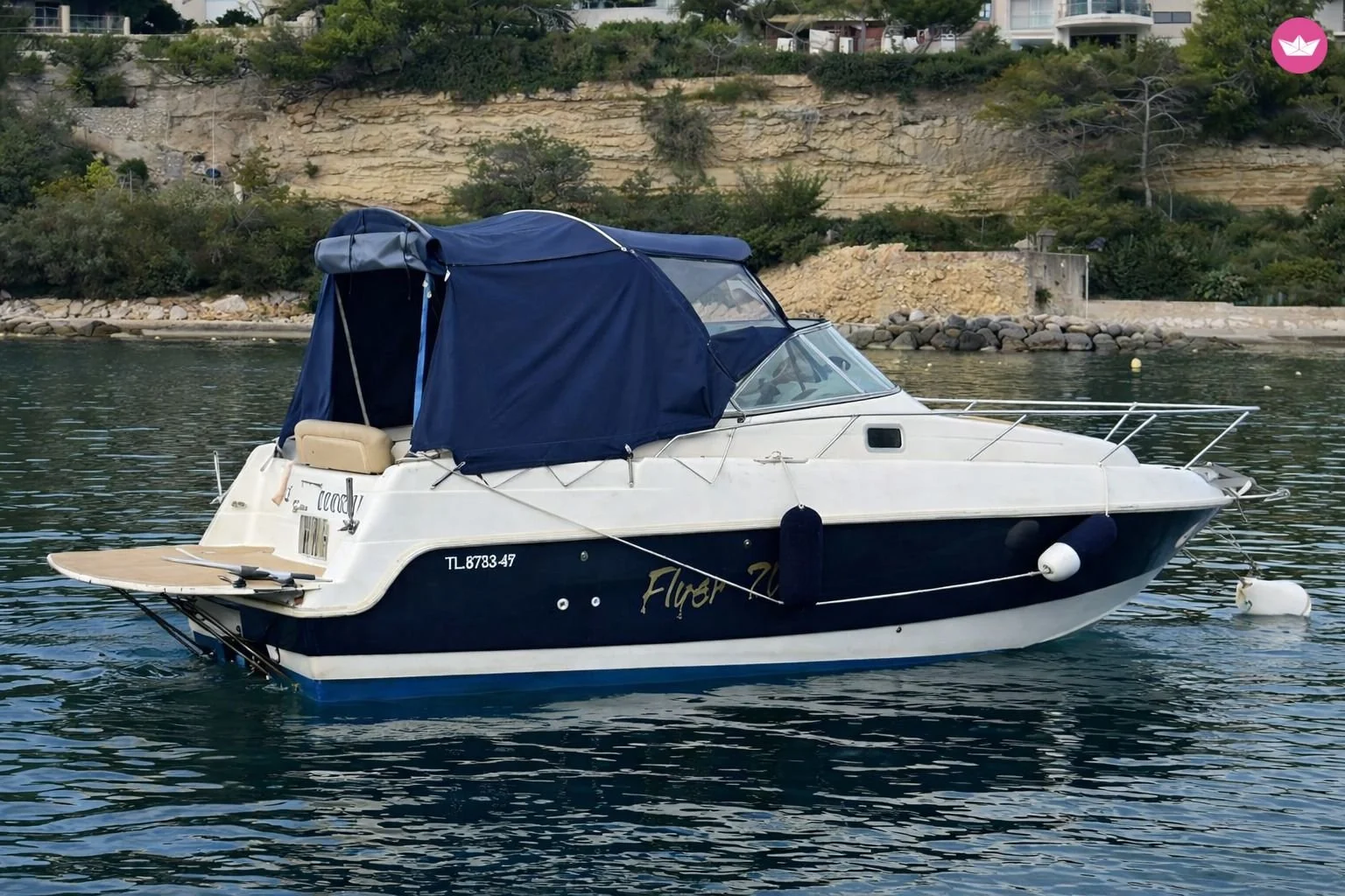 Bateau à moteur blanc et bleu avec une cabine bleue, amarré dans une eau calme près d'une côte rocheuse avec des maisons en arrière-plan. Location, bateau, plaisance, cote bleue, carry le rouet, sausset les pins, fos sur mer, martigues, carro.