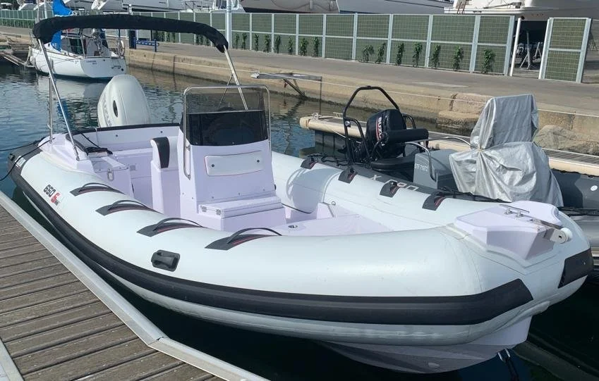 Bateau gonflable blanc avec un moteur hors-bord, amarré au quai, avec un autre bateau en arrière-plan. Location, bateau, plaisance, cote bleue, carry le rouet, sausset les pins, fos sur mer, martigues, carro.