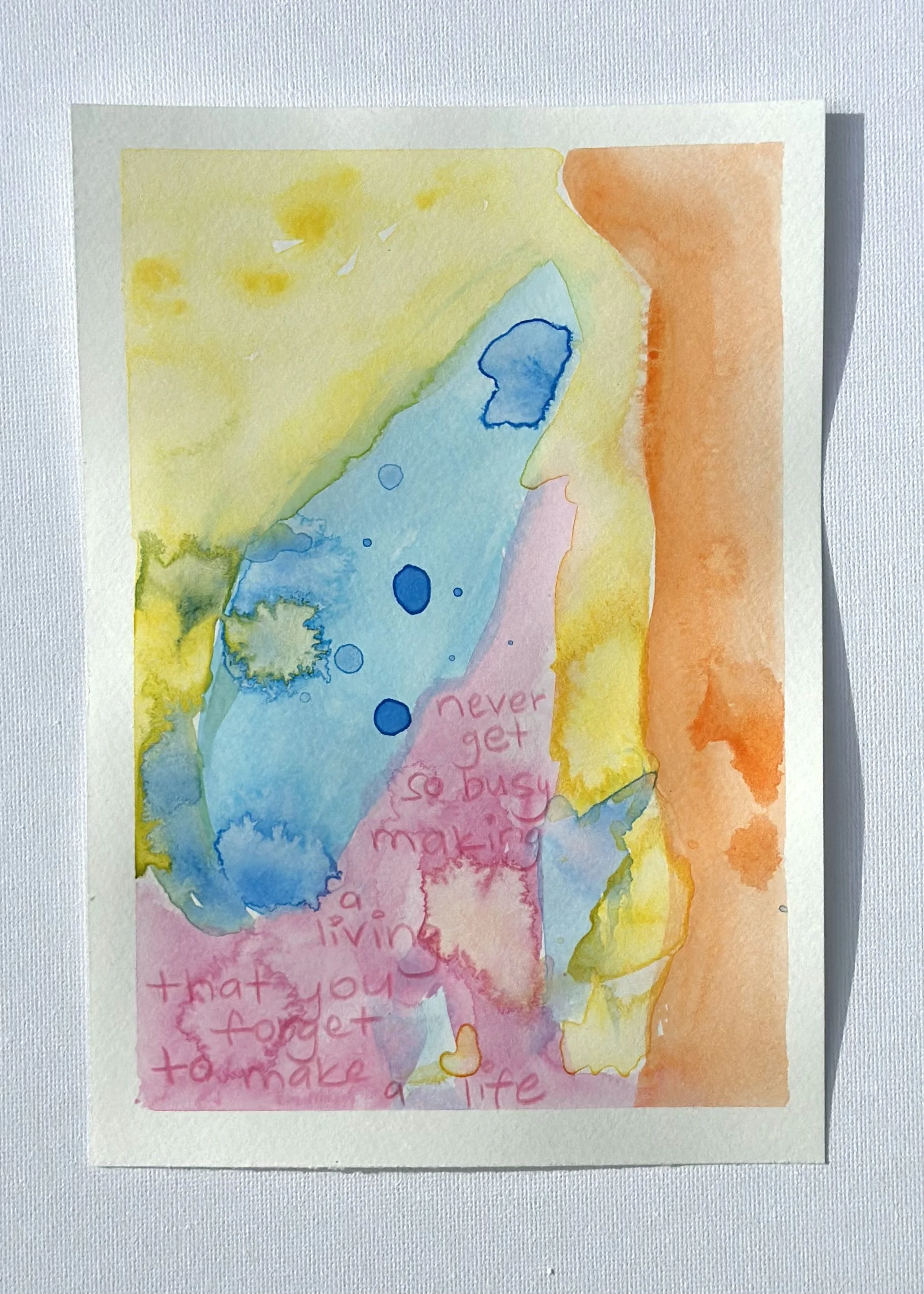 Watercolor painting with shades of yellow, blue, pink, and orange. There is a handwritten message in pink that says, 'Never get so busy making a living that you forget to make a life.'